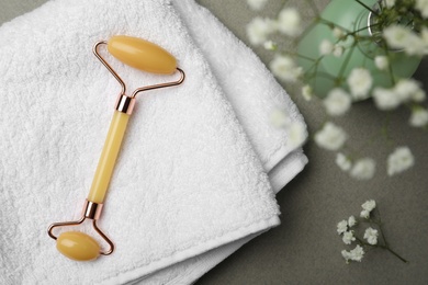 Photo of Natural jade face roller, towel and flowers on grey background, flat lay