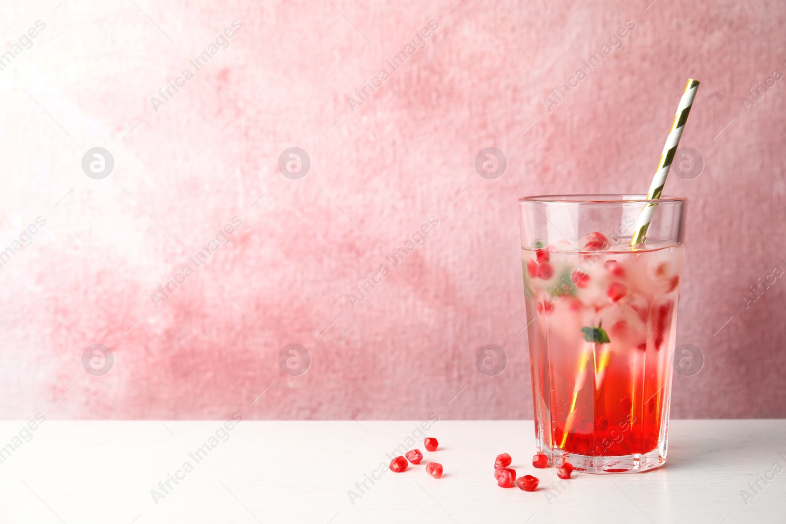 Photo of Tasty cocktail with pomegranate ice cubes on table against color background. Space for text