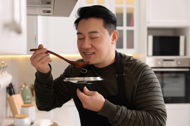Photo of Cooking process. Man tasting dish in kitchen