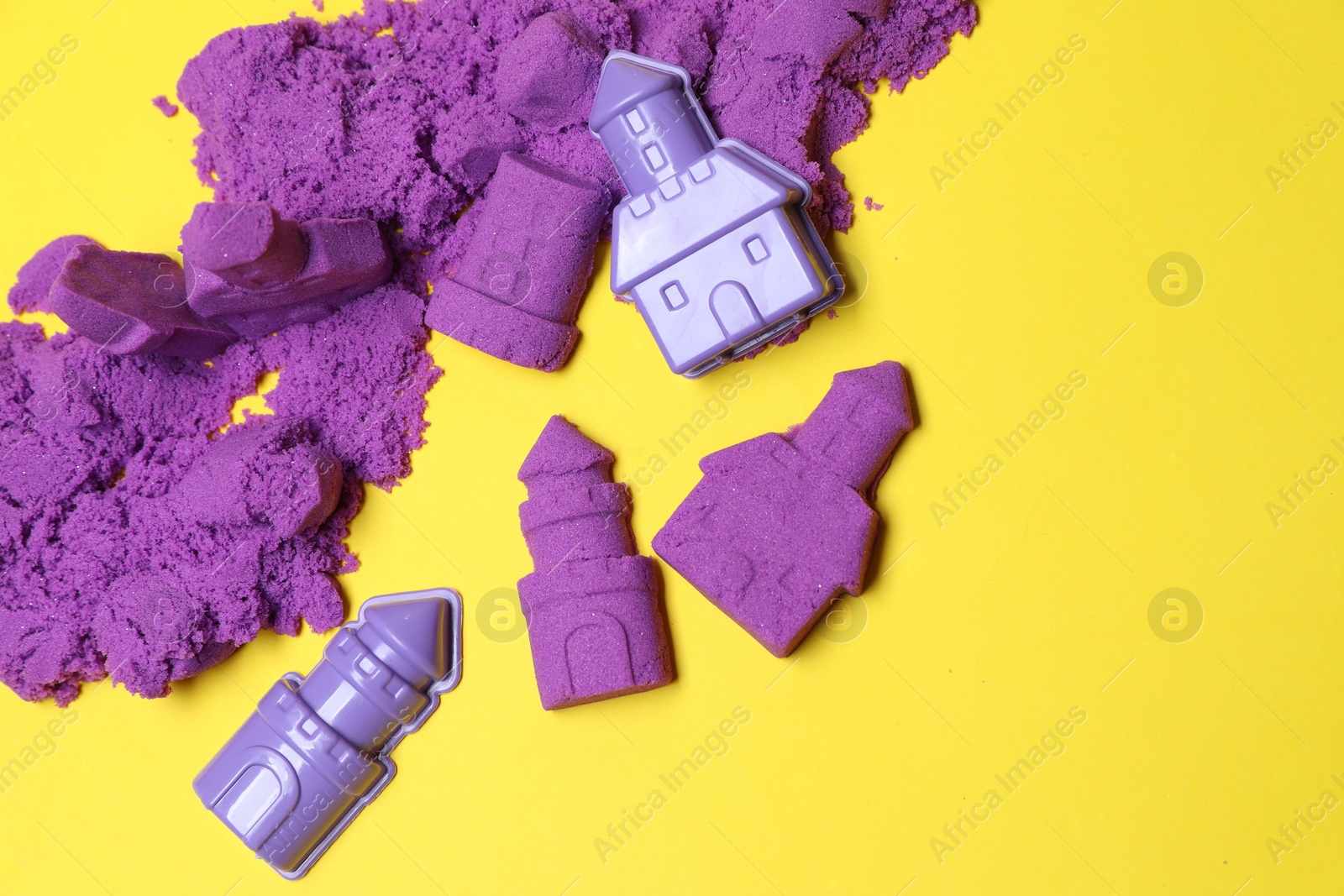 Photo of Castle figures made of kinetic sand and plastic toys on yellow background, flat lay. Space for text