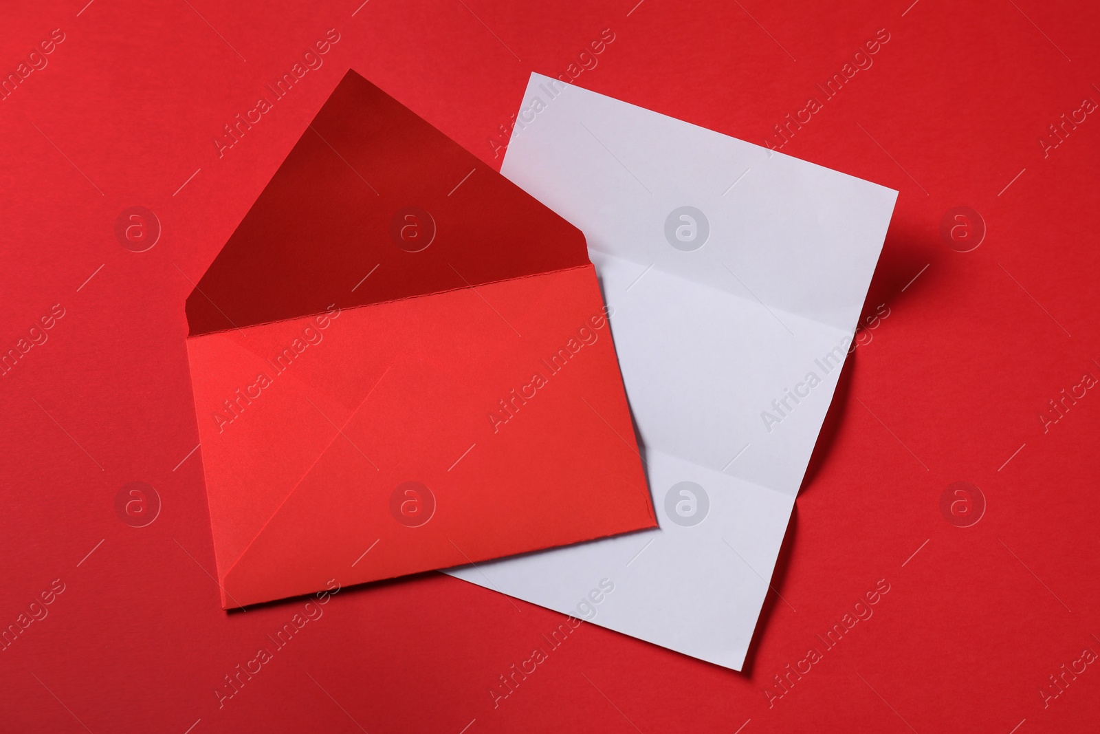 Photo of Blank sheet of paper and letter envelope on red background, top view. Space for text