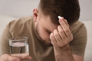 Photo of Man with glass of water and pill suffering from migraine, closeup