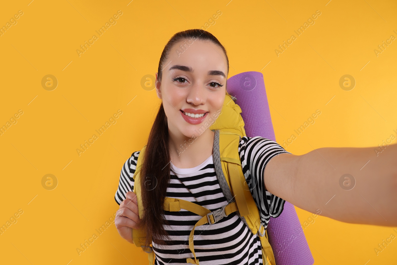 Photo of Smiling young woman with backpack taking selfie on orange background. Active tourism