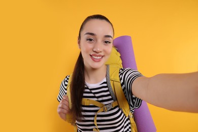 Photo of Smiling young woman with backpack taking selfie on orange background. Active tourism