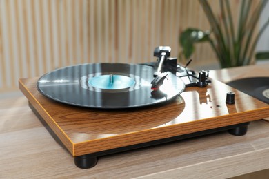 Photo of Stylish turntable with vinyl disc on wooden table indoors