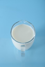 Jug of fresh milk on light blue background, above view