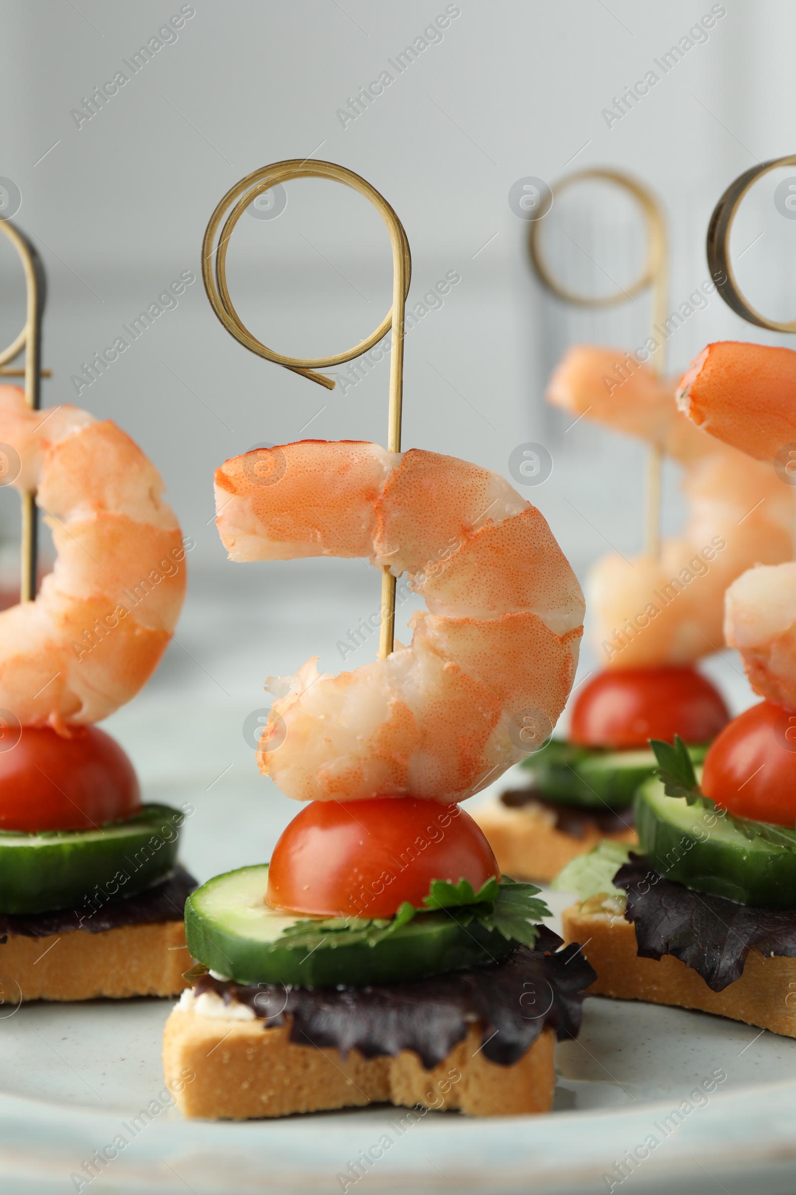 Photo of Tasty canapes with shrimps, cucumber, greens and tomatoes on plate, closeup