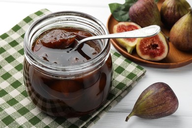 Photo of Jar of tasty sweet fig jam on white wooden table