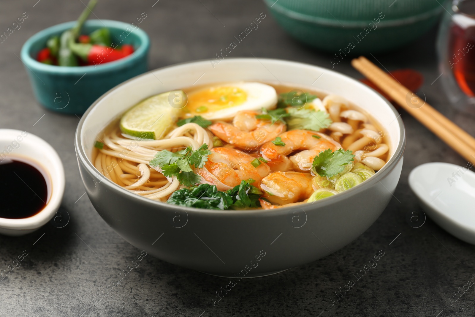 Photo of Delicious ramen with shrimps and egg in bowl on grey table, closeup. Noodle soup