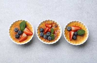 Delicious creme brulee with berries and mint in bowl on grey textured table, top view