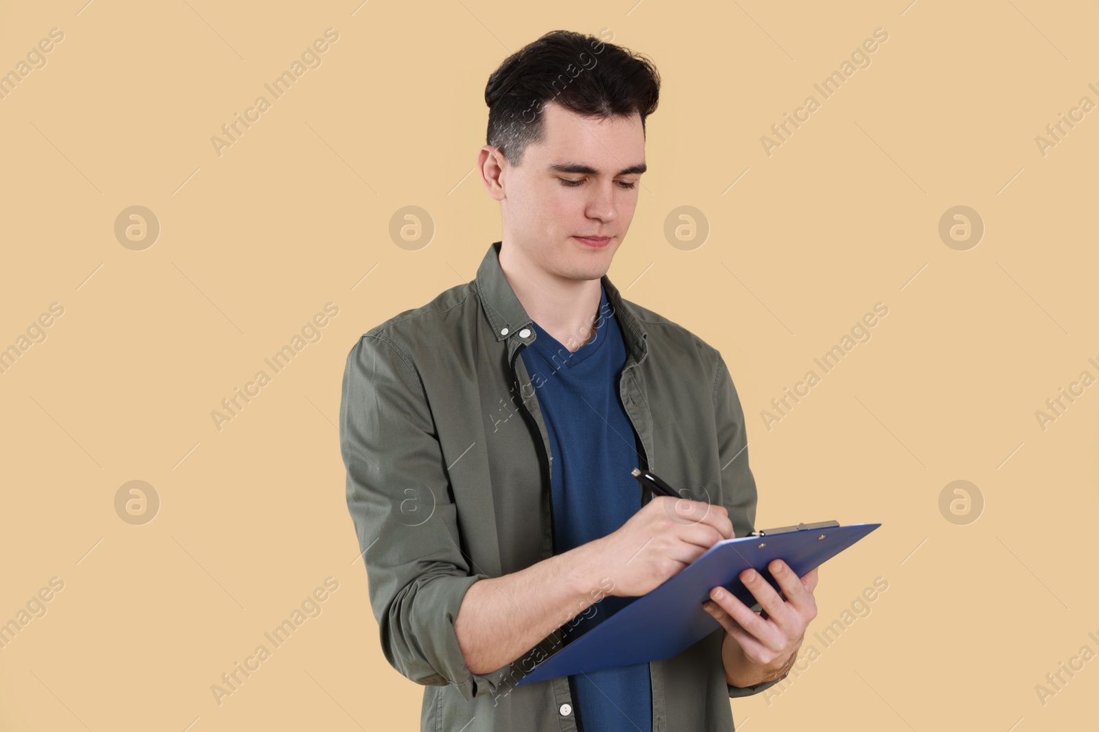 Photo of Handsome young man writing on clipboard against beige background
