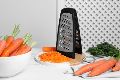 Photo of Tasty ripe carrots with grater on white table indoors
