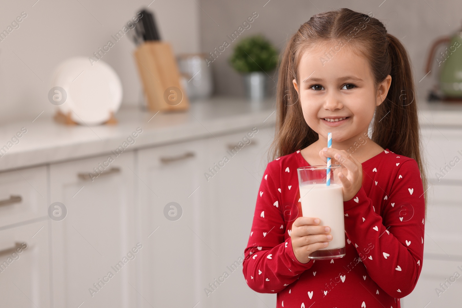 Photo of Cute girl with glass of fresh milk in kitchen, space for text