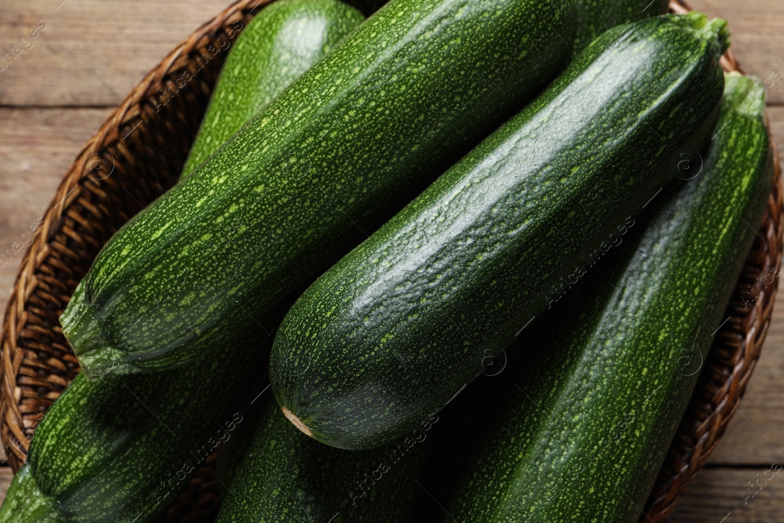 Photo of Raw ripe zucchinis in wicker basket on table, top view