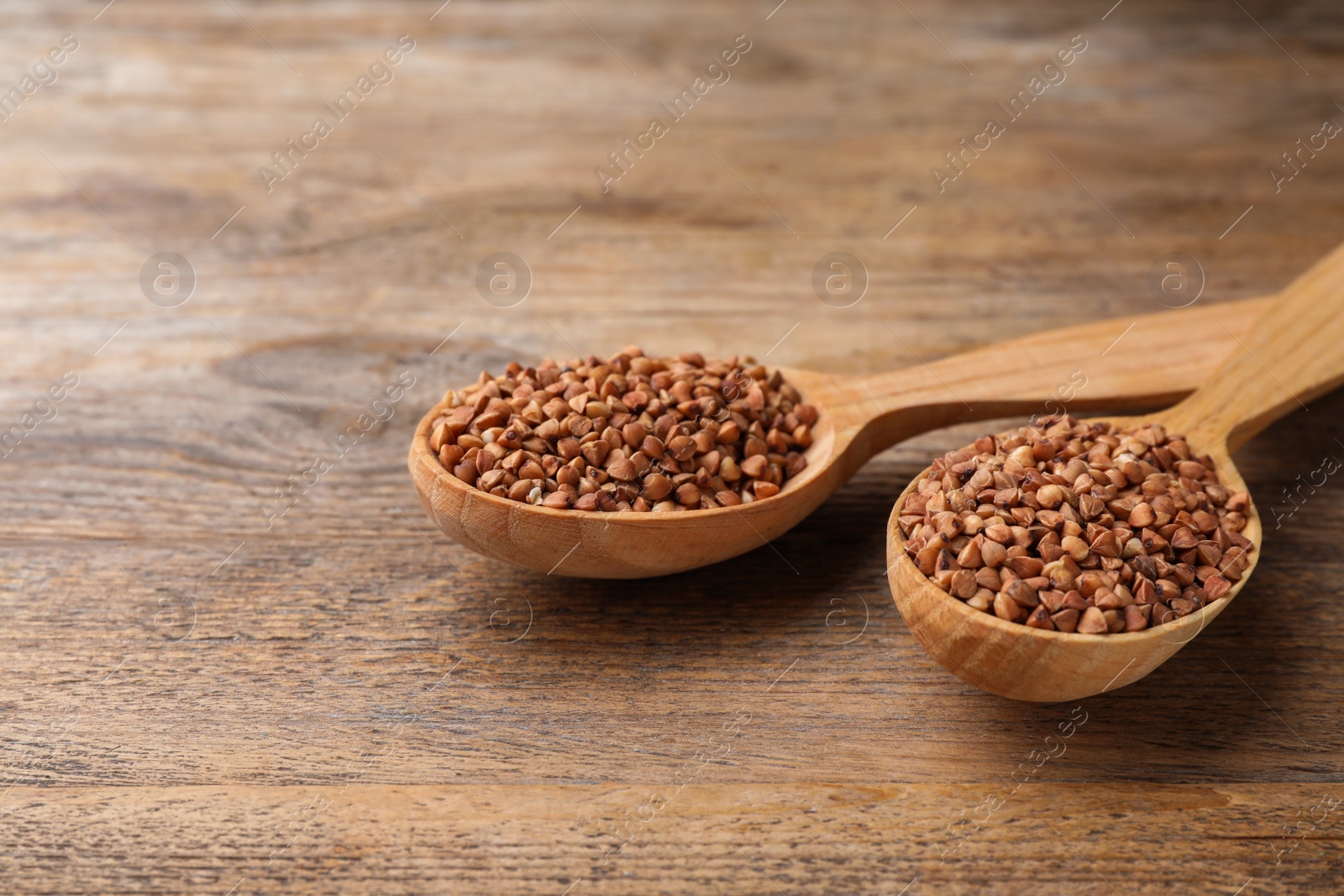 Photo of Buckwheat grains in spoons on wooden table