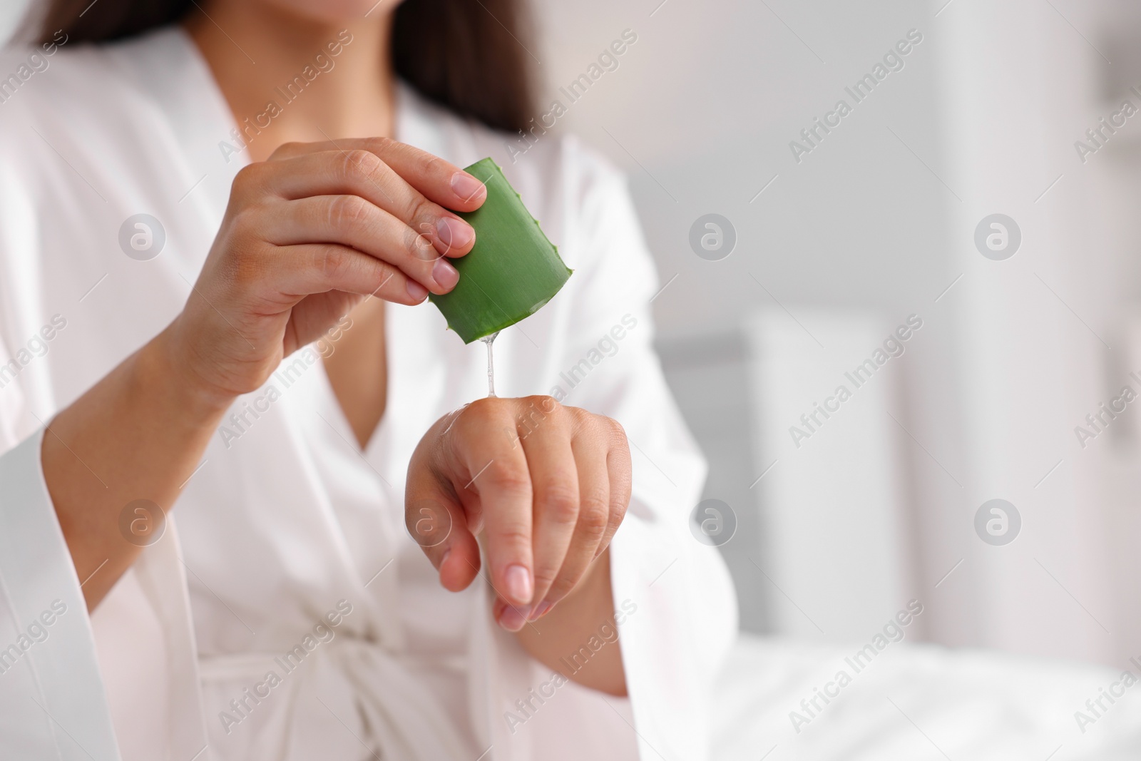 Photo of Young woman applying aloe gel from leaf onto her hand indoors, closeup. Space for text