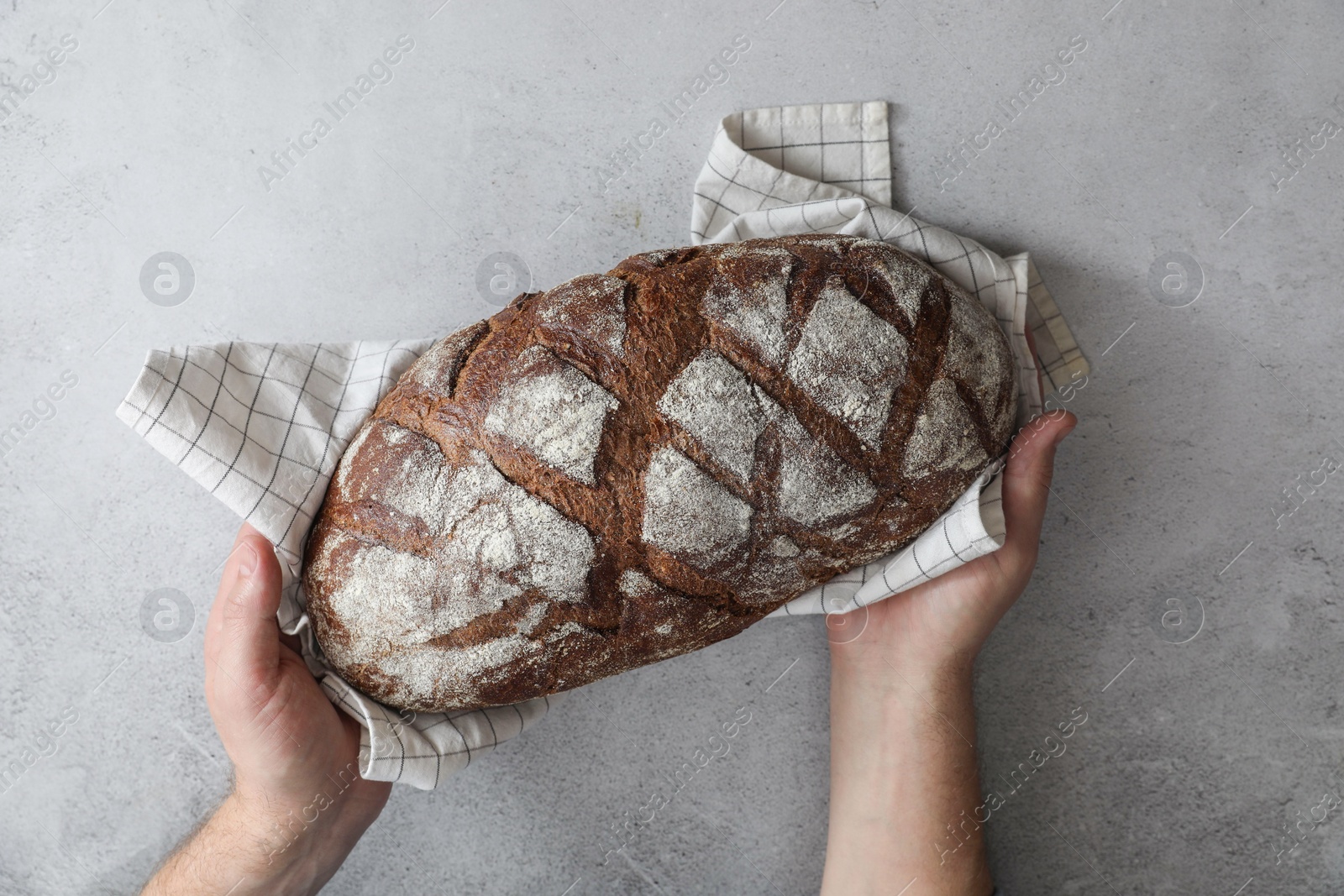 Photo of Man holding loaf of fresh bread at grey table, top view