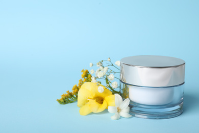 Jar of luxury face cream and flowers on light blue background. Space for text