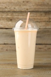 Photo of Plastic cup of tasty smoothie on wooden table