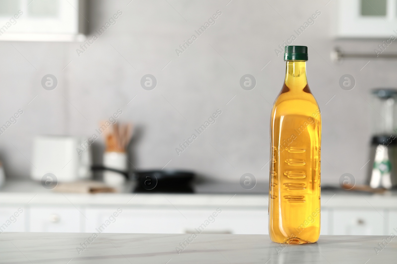 Photo of Bottle of cooking oil on white marble table in kitchen. Space for text