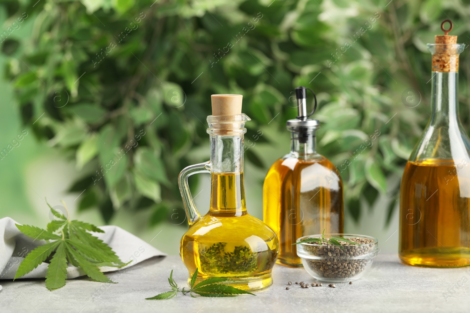 Photo of Hemp oil, seeds and leaves on grey table against blurred background