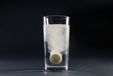 Effervescent pill dissolving in glass of water on grey table