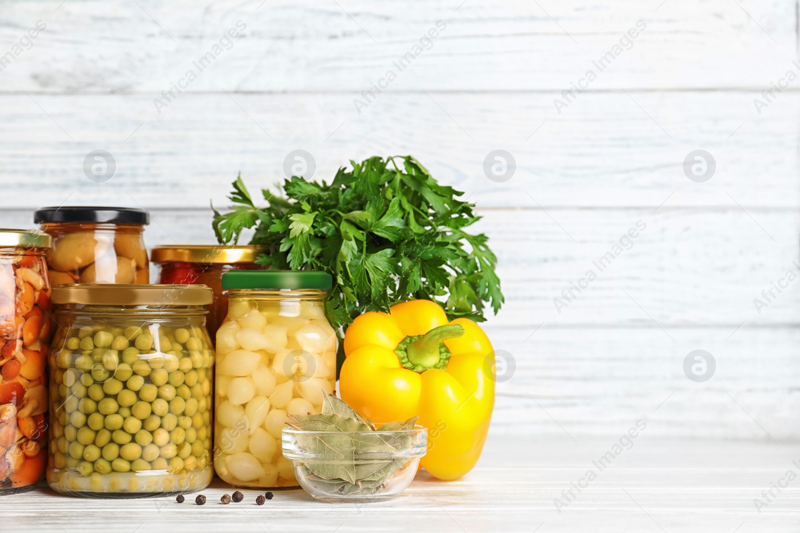 Photo of Glass jars with different pickled vegetables on white wooden table. Space for text