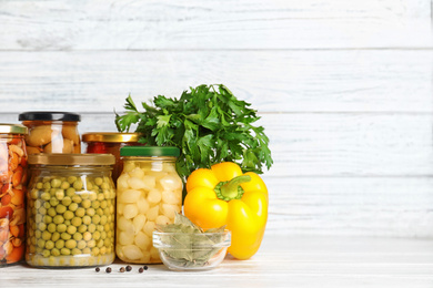 Glass jars with different pickled vegetables on white wooden table. Space for text