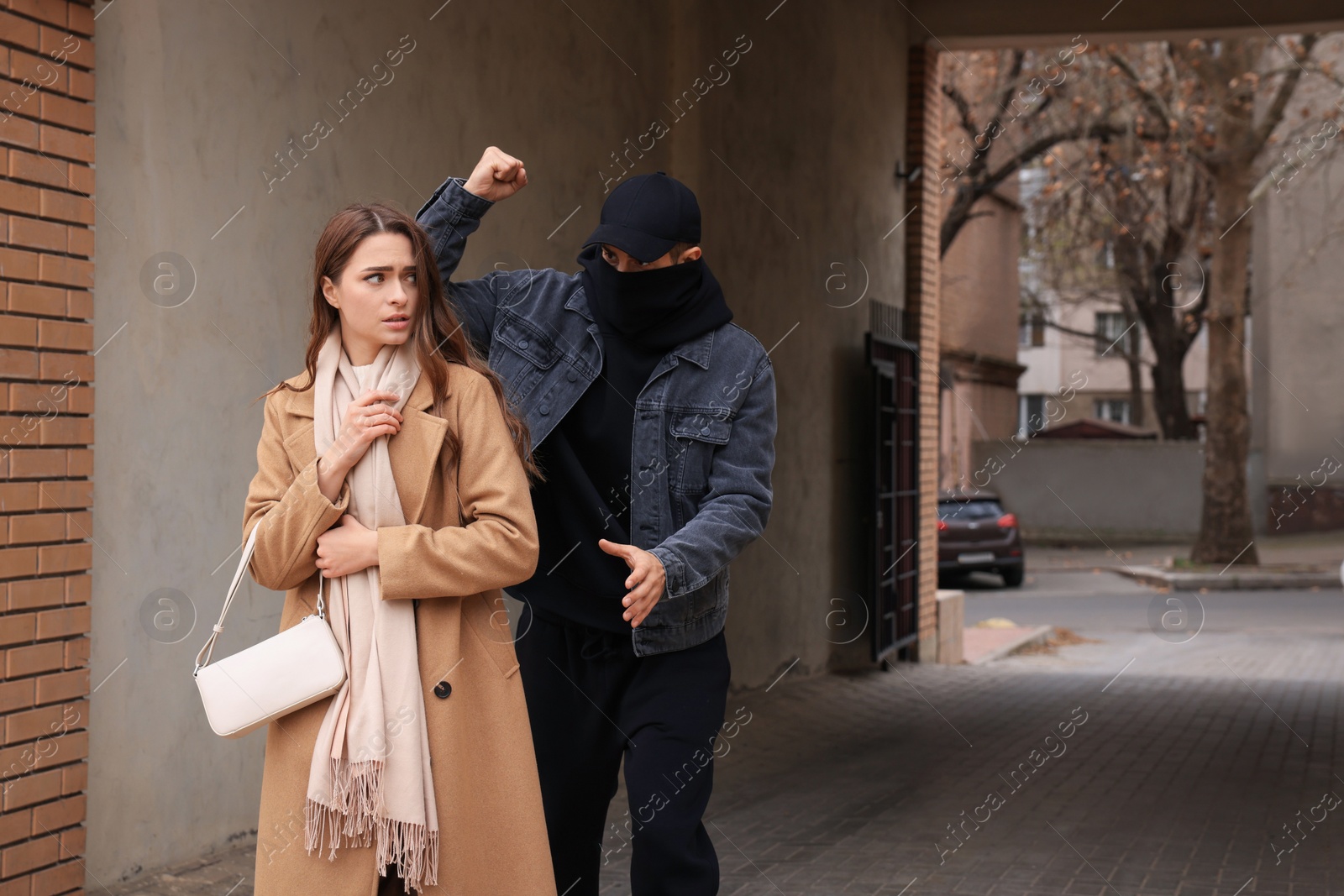 Photo of Criminal attacking young woman in alley, space for text. Self defense concept