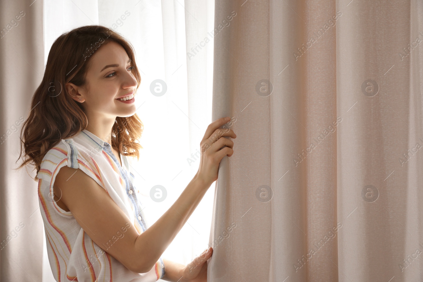 Photo of Woman opening window curtains at home in morning