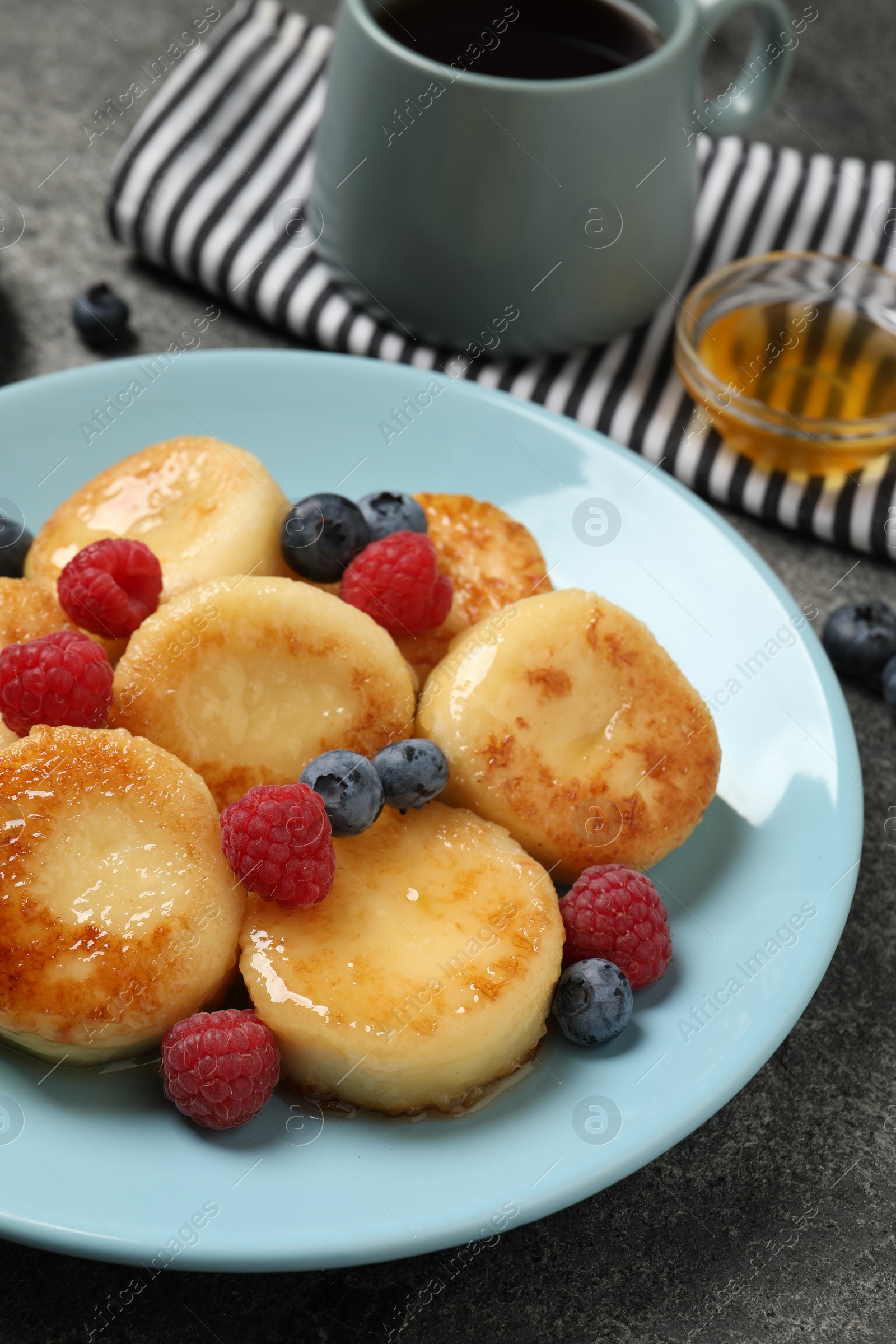 Photo of Delicious cottage cheese pancakes with fresh berries and honey on grey table, closeup