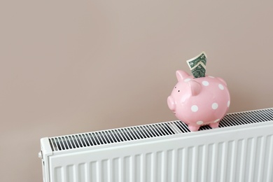 Photo of Heating radiator with piggy bank and money near color wall. Space for text