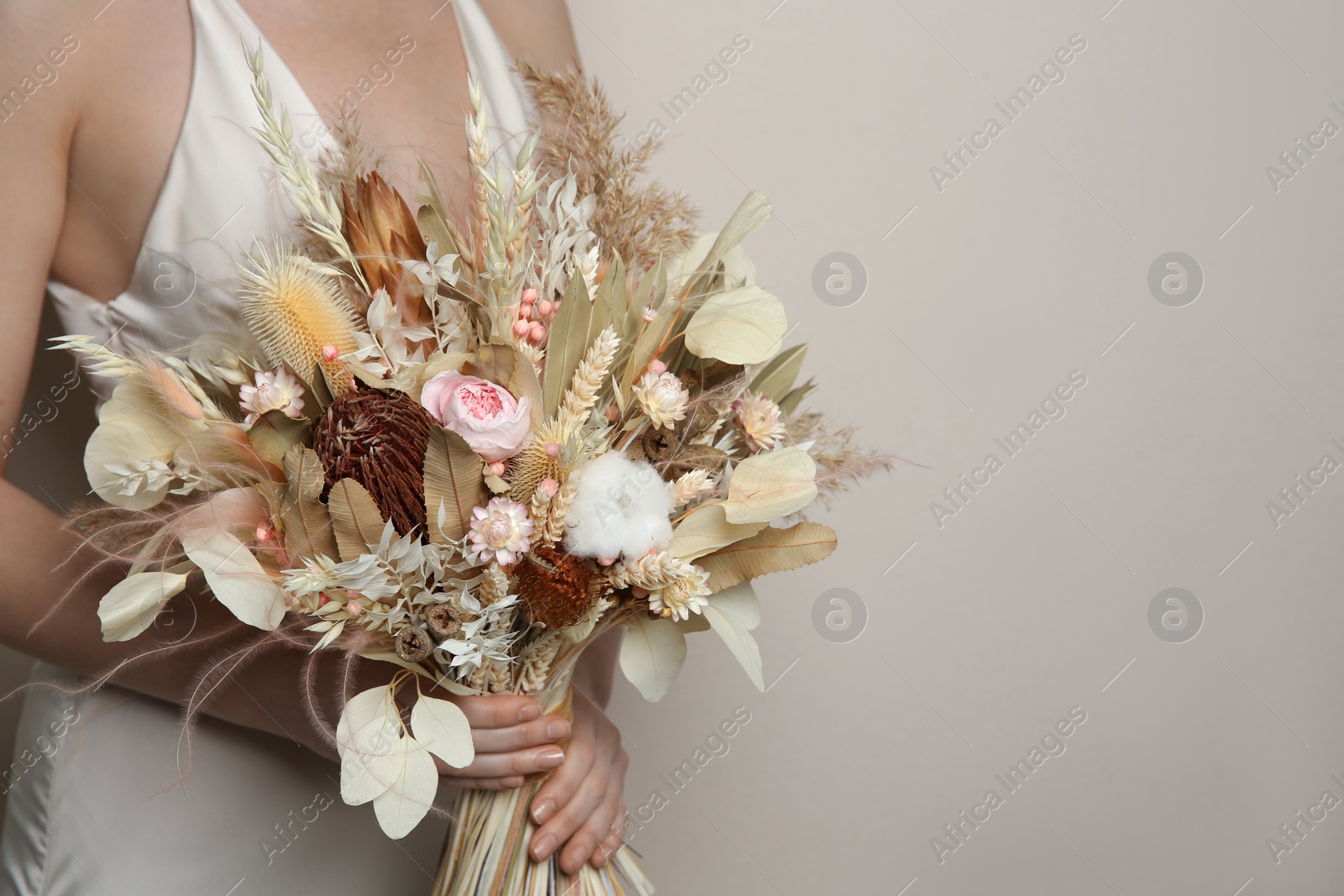Photo of Bride holding beautiful dried flower bouquet on beige background, closeup. Space for text