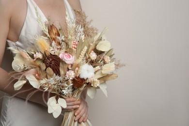 Bride holding beautiful dried flower bouquet on beige background, closeup. Space for text