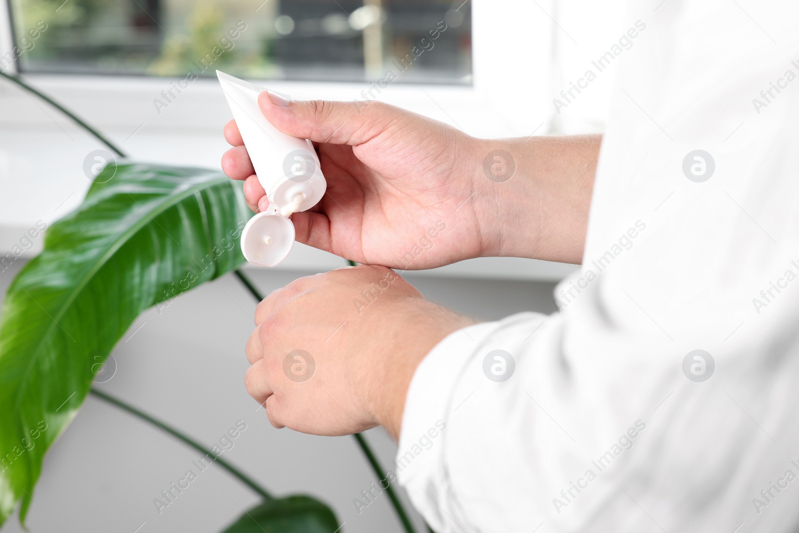 Photo of Man applying hand cream from tube at home, closeup