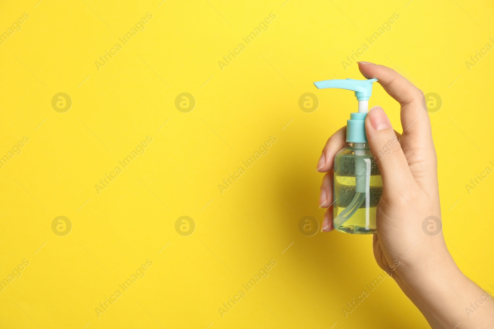 Photo of Woman holding antiseptic gel on yellow background, closeup. Space for text