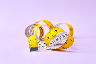 New measuring tape on violet background, closeup