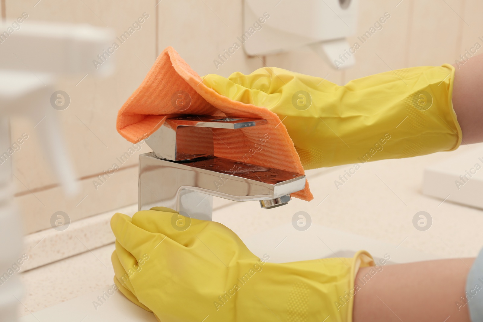 Photo of Woman cleaning faucet with rag in bathroom, closeup