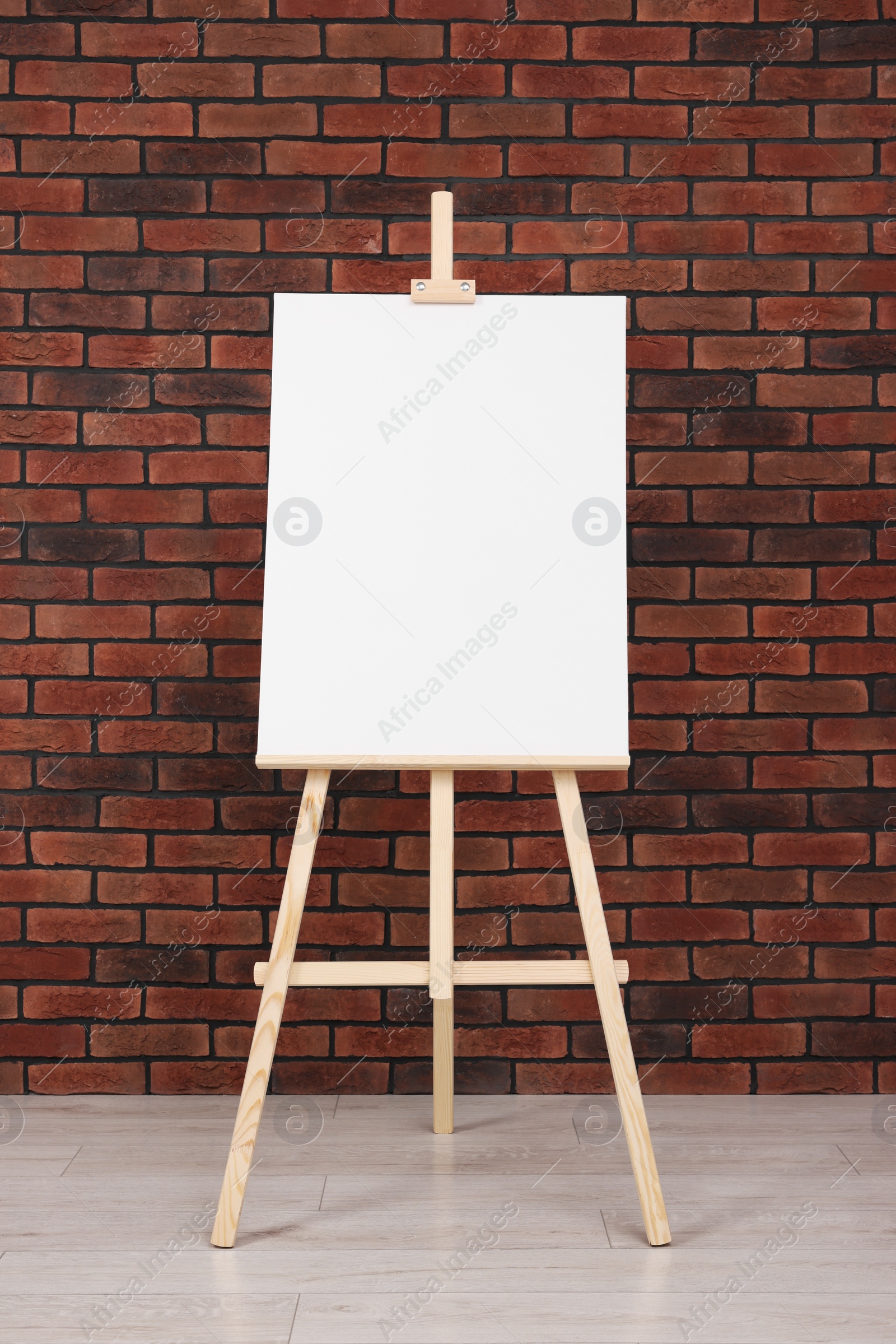 Photo of Wooden easel with blank canvas near brick wall indoors