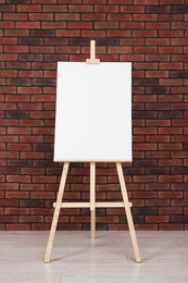 Wooden easel with blank canvas near brick wall indoors