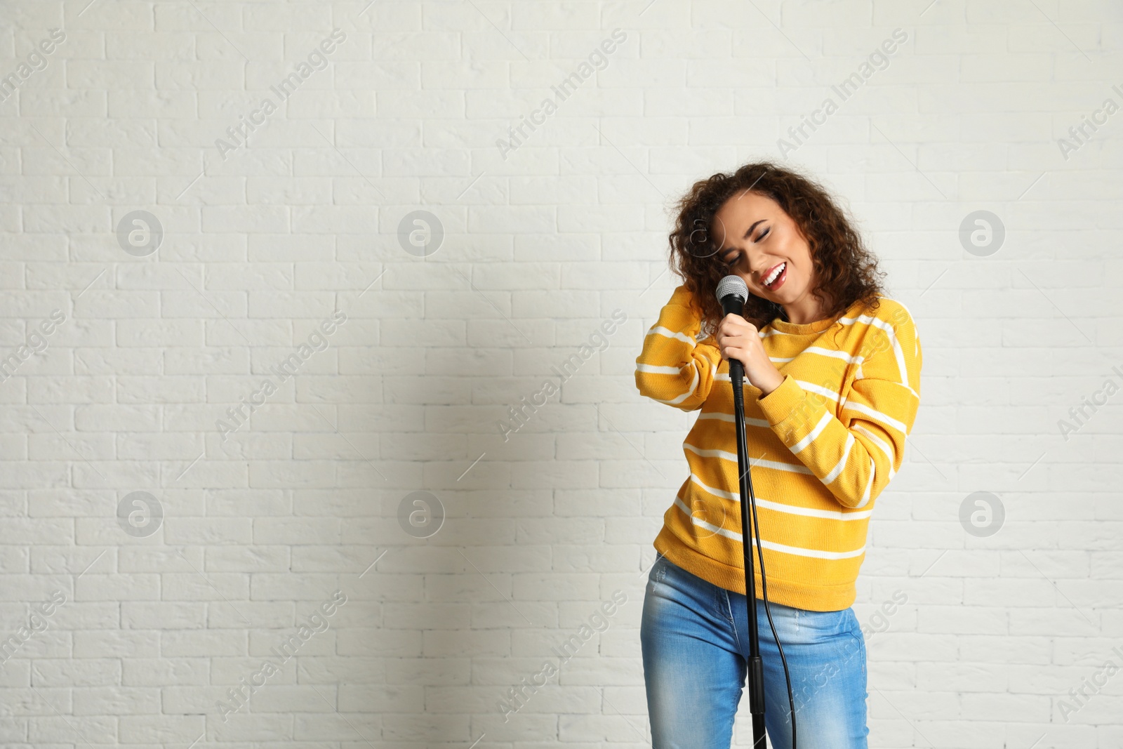 Photo of Portrait of curly African-American woman singing in microphone near brick wall. Space for text