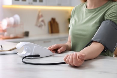 Photo of Woman measuring blood pressure in kitchen, closeup. Space for text
