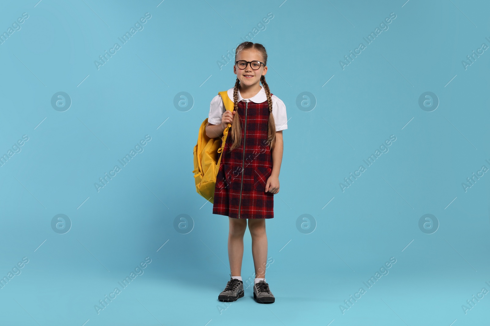 Photo of Happy schoolgirl in glasses with backpack on light blue background