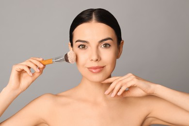 Photo of Beautiful young woman applying face powder with brush on grey background