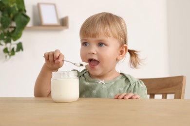 Photo of Cute little child eating tasty yogurt with spoon at wooden table indoors