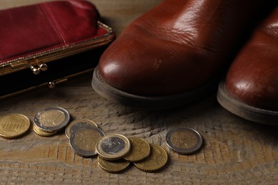Poverty. Old boots, wallet and coins on wooden table, closeup