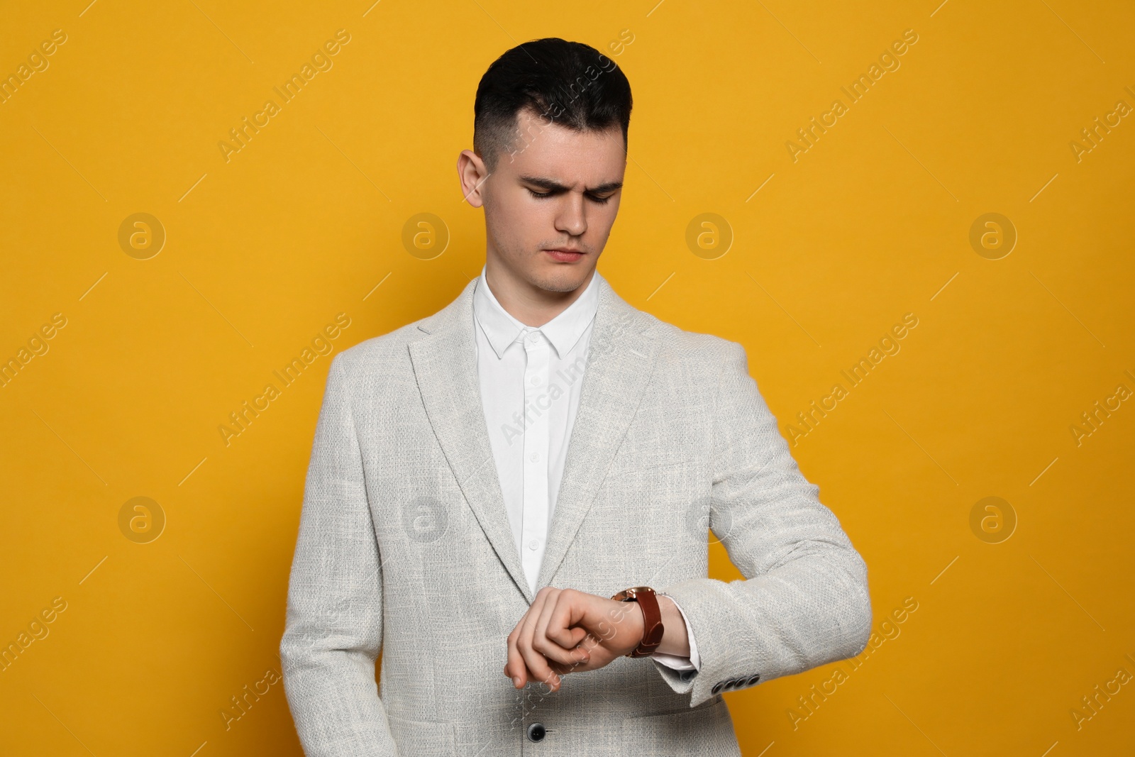 Photo of Young man checking time on orange background. Being late concept