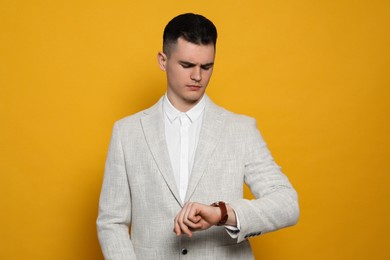 Photo of Young man checking time on orange background. Being late concept