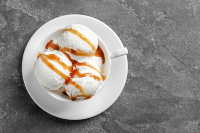 Tasty ice cream with caramel sauce in mug on gray background, top view
