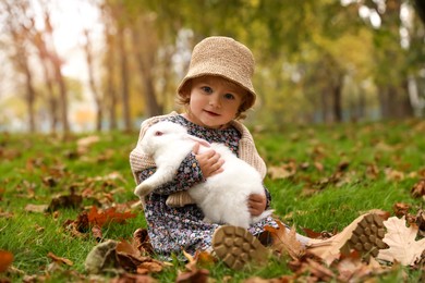 Photo of Girl sitting with cute white rabbit on grass in autumn park